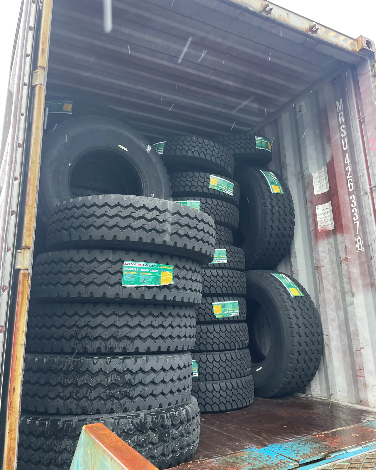 New truck tires with green labels stacked in columns inside an open shipping container