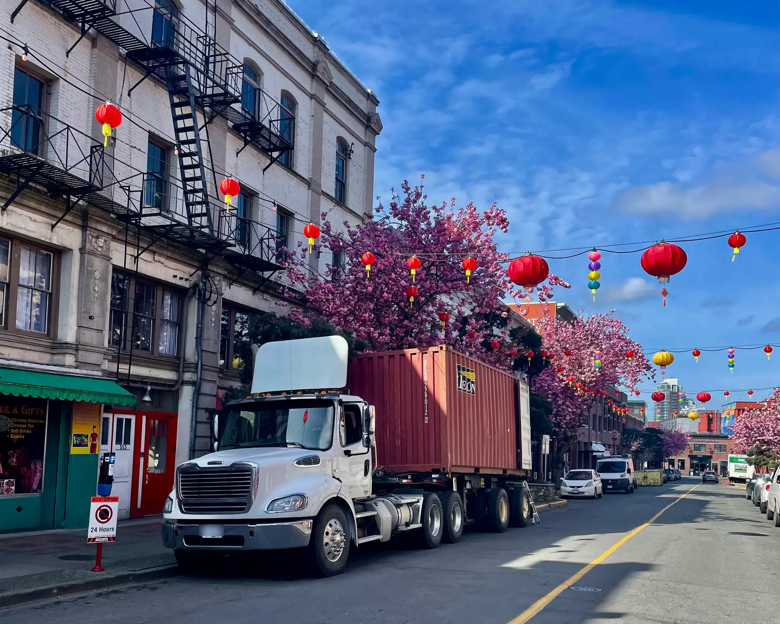 A tractor and container parked on a downtown street lined with heritage buildings, red lanterns and cherry blossoms